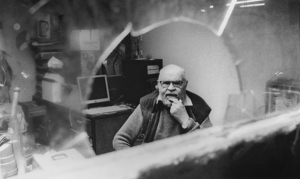Shopkeeper behind the window of his cluttered repair shop