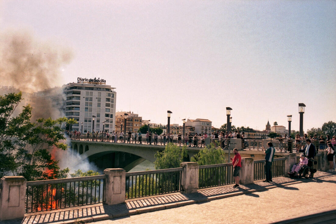 Crowd on a Seville bridge watching smoke rise over the river