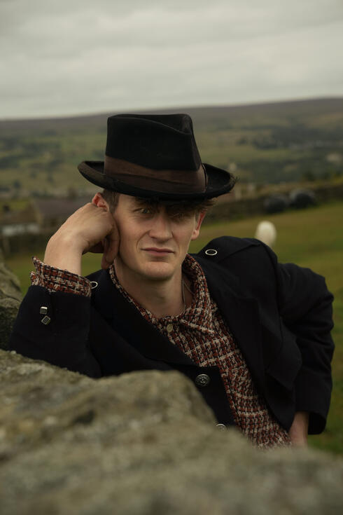 Member of The Homburgs in hat and coat on a hillside