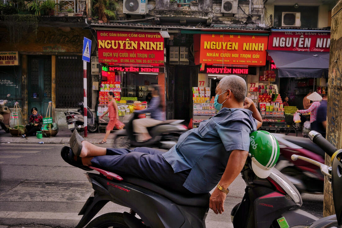 Man relaxing on his parked scooter outside Hanoi shops