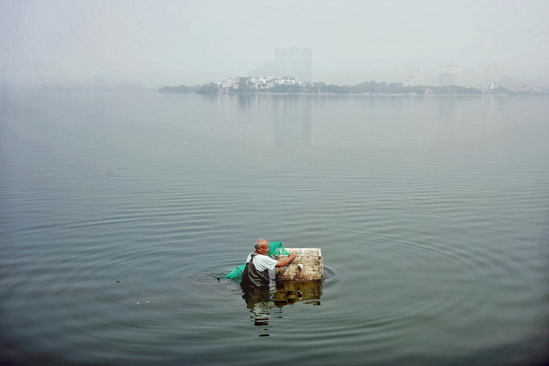 Man wading through misty West Lake at dawn, Hanoi
