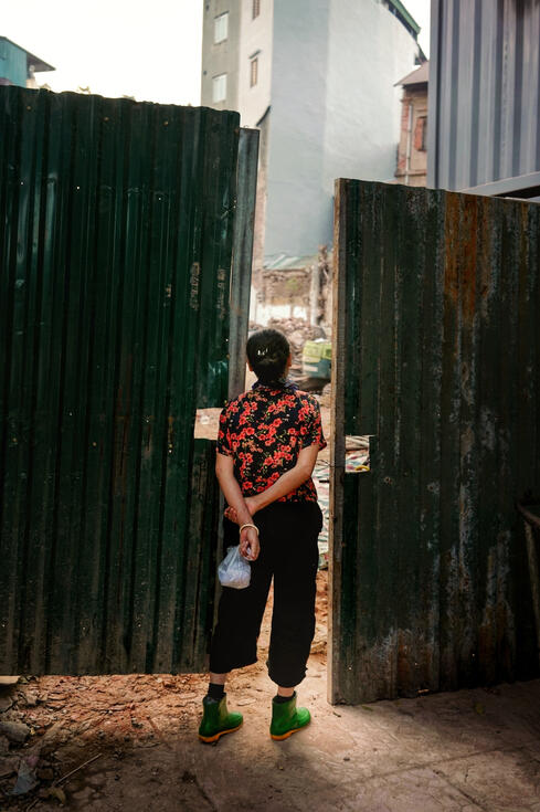 Woman in a floral shirt beside a corrugated demolition gate, Hanoi
