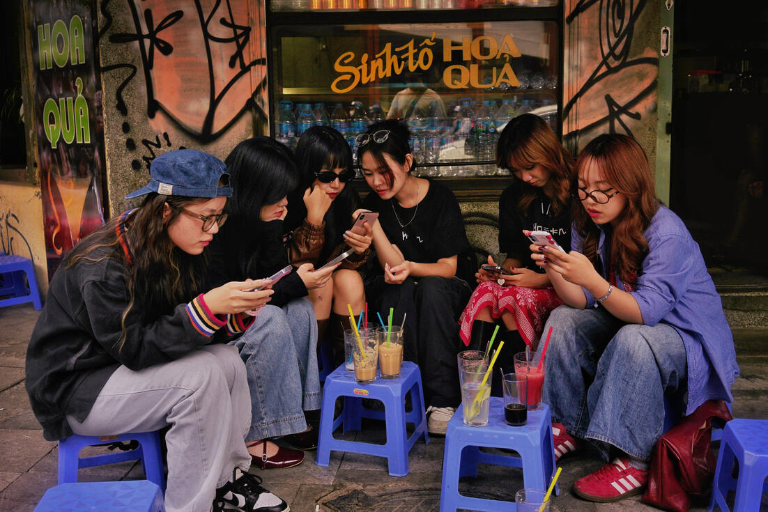 Young women on their phones at a Hanoi street smoothie bar
